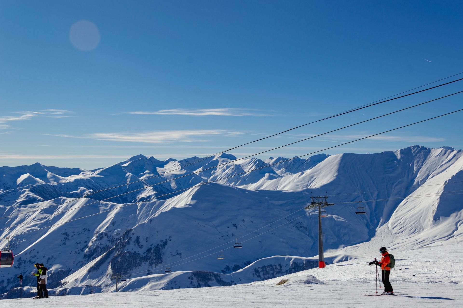 Skiers on the sunny upper slopes of Gudauri with the snow-covered Caucasus behind