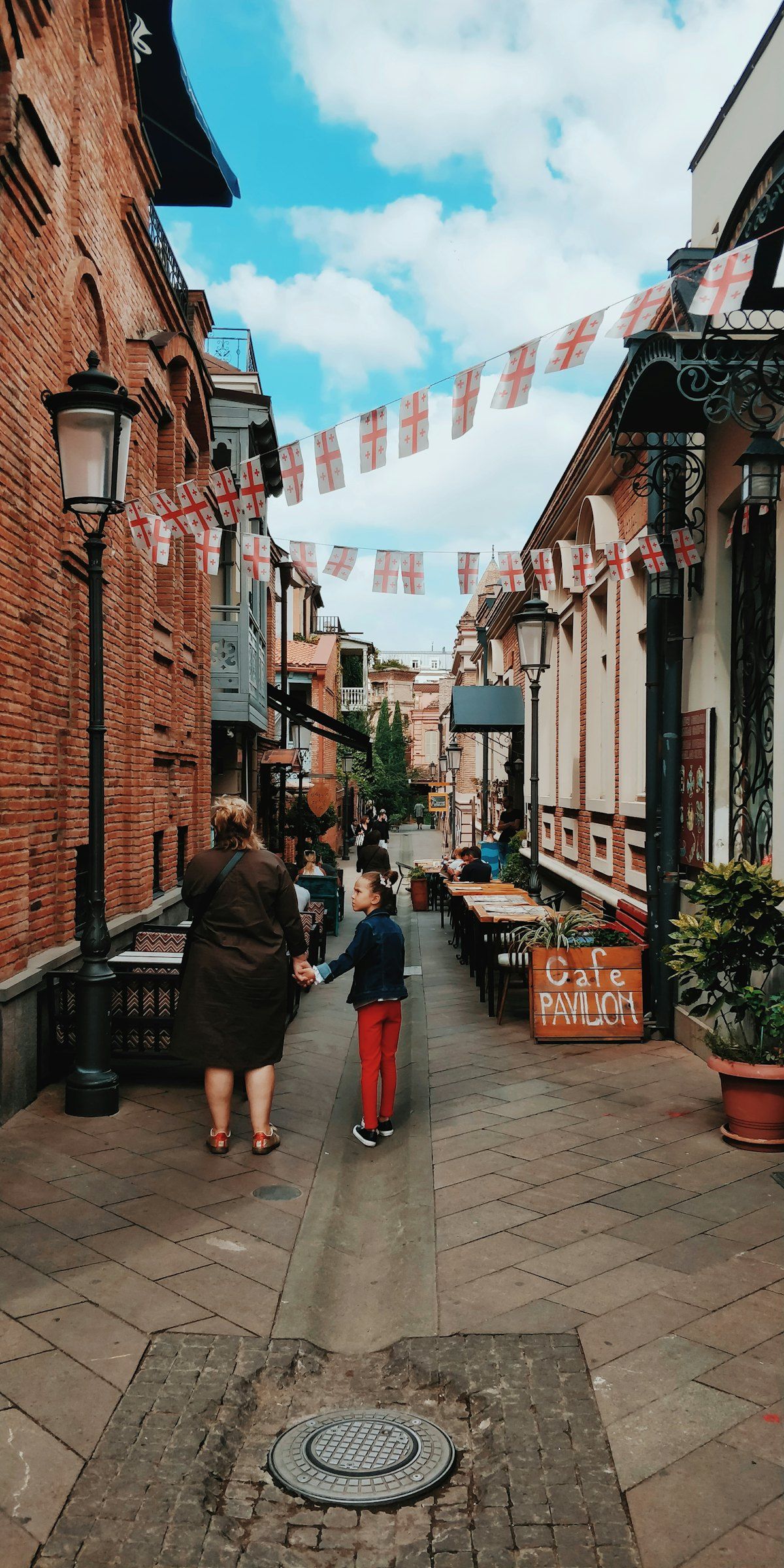 A grandmother and granddaughter walking hand in hand down a quiet old Tbilisi lane